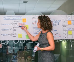 Portrait of female coach showing project management studies on paper over glass wall in headquarters