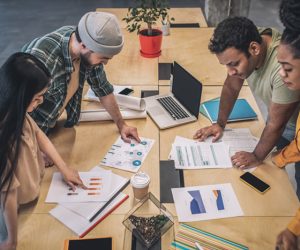 Brainwork. Group of young interracial focused people discussing schemes and diagrams standing at large table while working on project in office